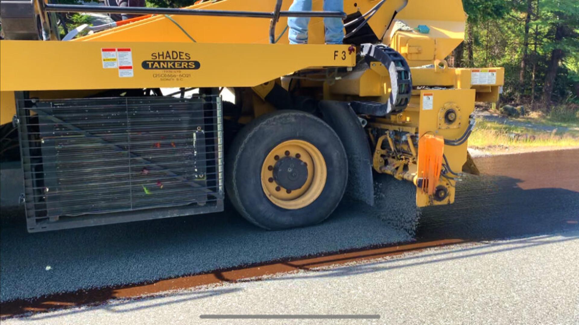 Asphalt paving machine distributing fresh asphalt on a roadway in a construction site.