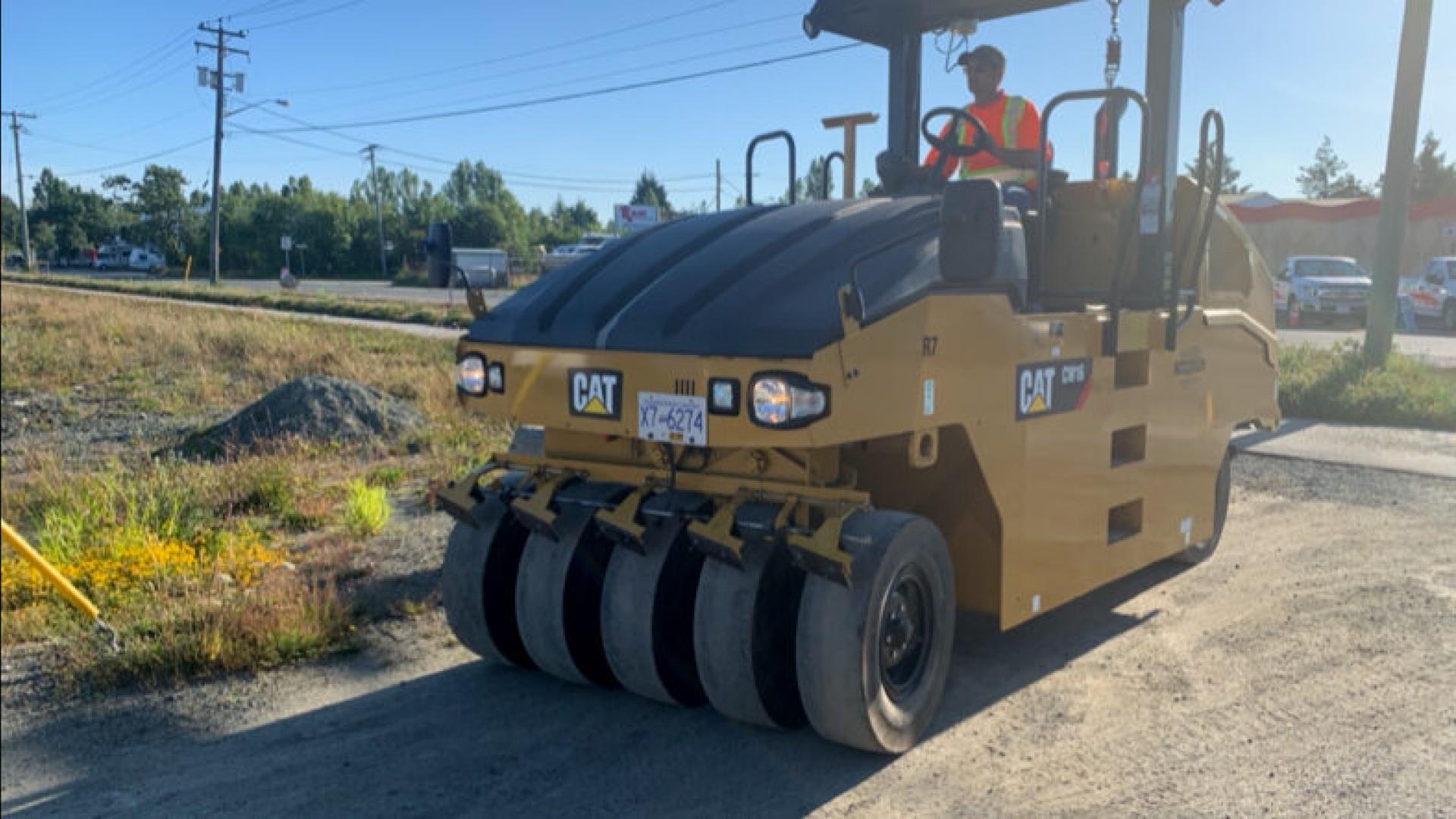 A large yellow roller compactor stationed on a construction site under a clear sky.