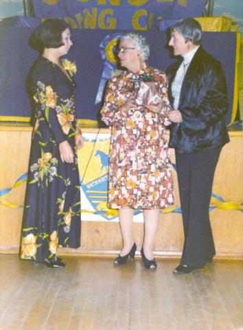 Three ladies in formal wear are standing together and chatting.