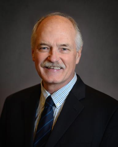 Professional headshot of a smiling individual in a suit and tie.