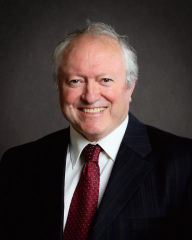Smiling person in a suit with a red tie against a dark background.