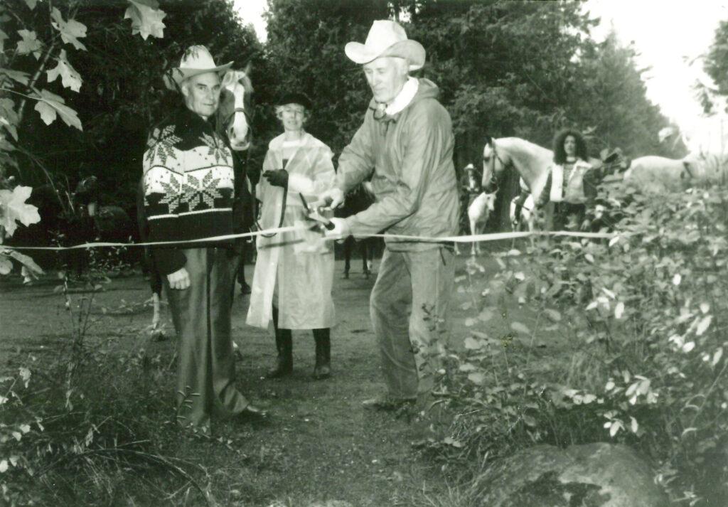 Two men in cowboy hats cut the official opening ribbon. Horses and riders in the background.