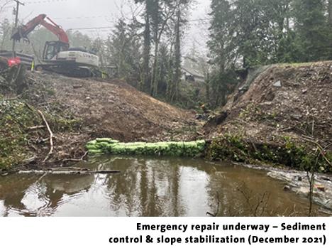 Construction equipment working on a slope stabilization project beside a foggy waterway.