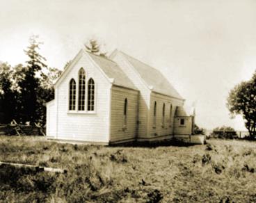 A weathered white church building surrounded by tall grass and trees.