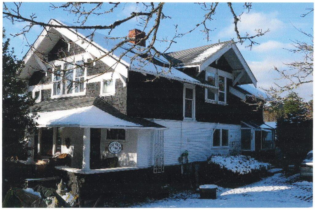 Two-storey house with black and white siding, surrounded by snow and trees under a blue sky.
