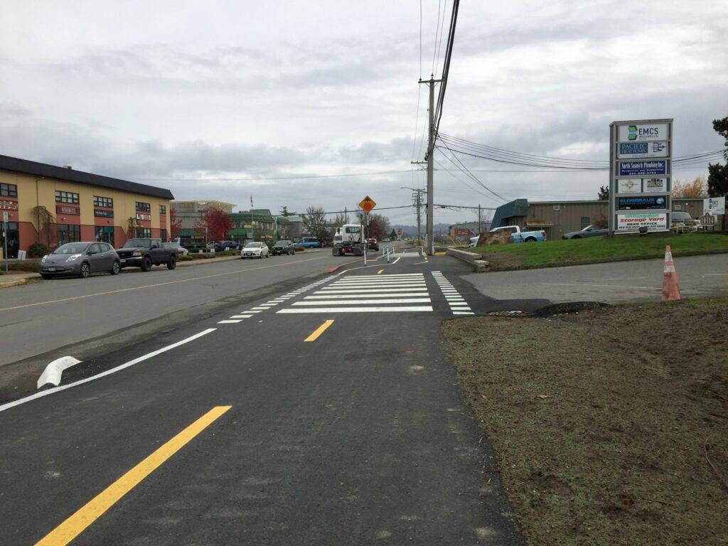 Newly paved cycle lane beside a road, with traffic and signs visible in the background.
