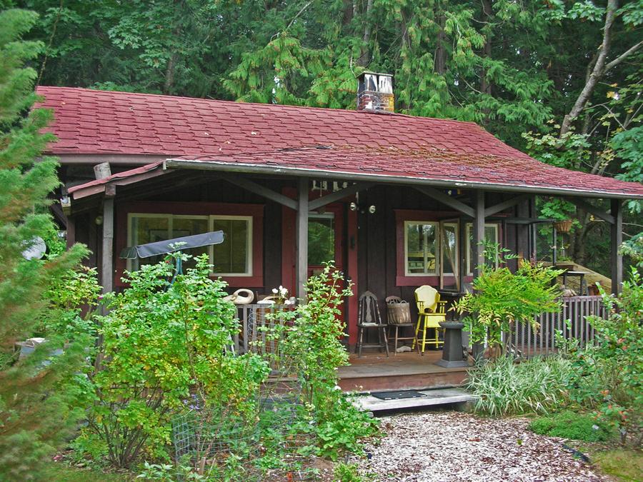 Cozy cabin surrounded by greenery, with a red roof and porch furniture.