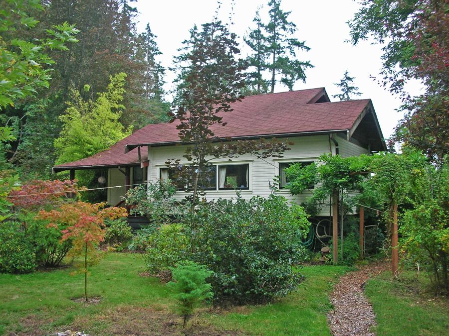 A quaint house surrounded by lush greenery and trees, with a garden pathway.