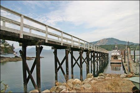 Wooden pier extending over calm water, with rocky shore and distant mountains.