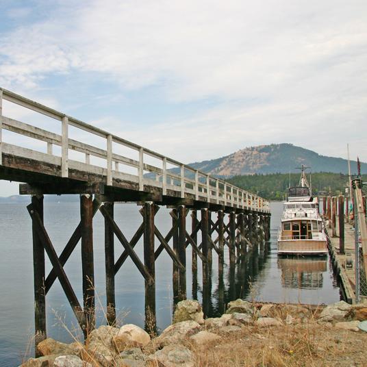 Wooden pier extending over calm water, with a boat docked nearby and mountains in the background.