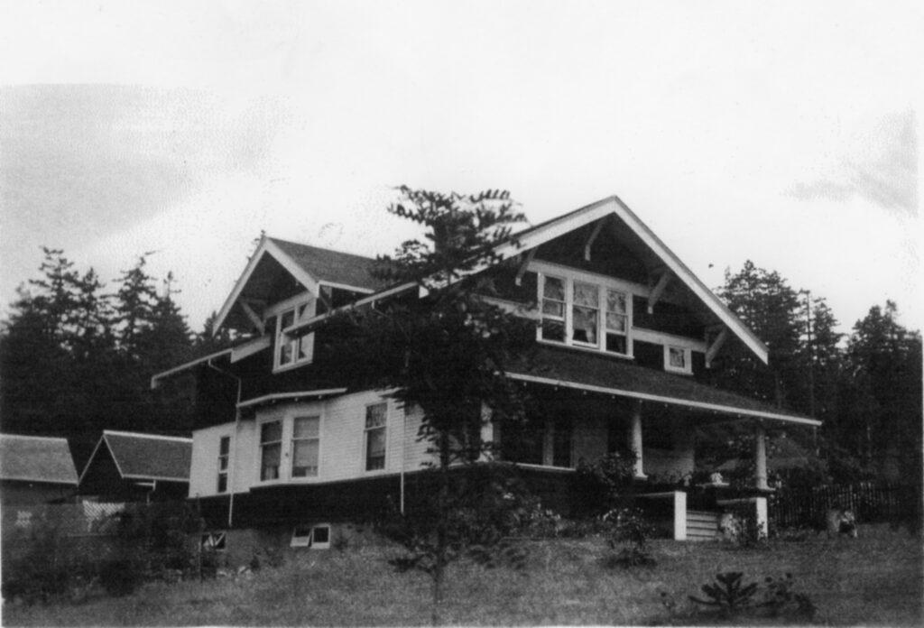 Historic two-storey house with a large porch, surrounded by trees and grassy land.