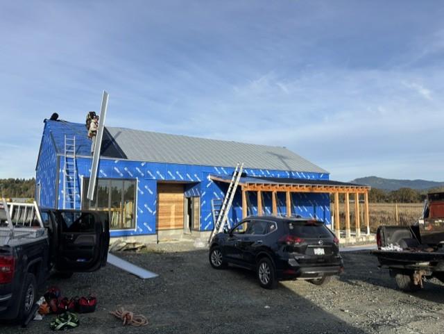 Front of a rectangular building under construction. A worker installs roofing panels.