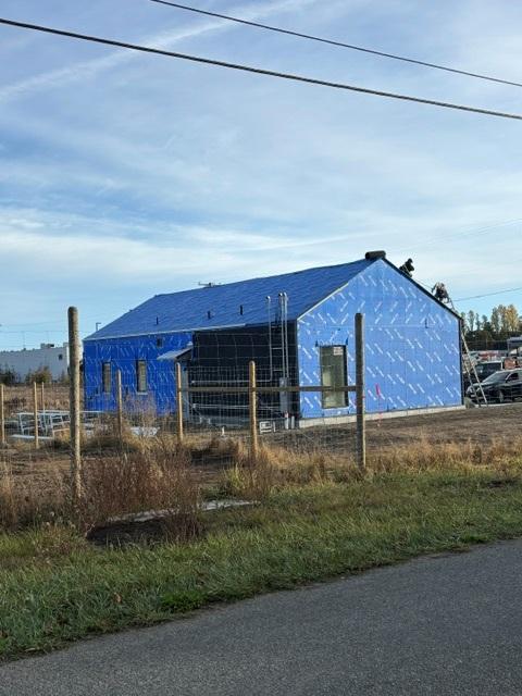 Back of a rectangular building under construction. A worker installs roofing panels.