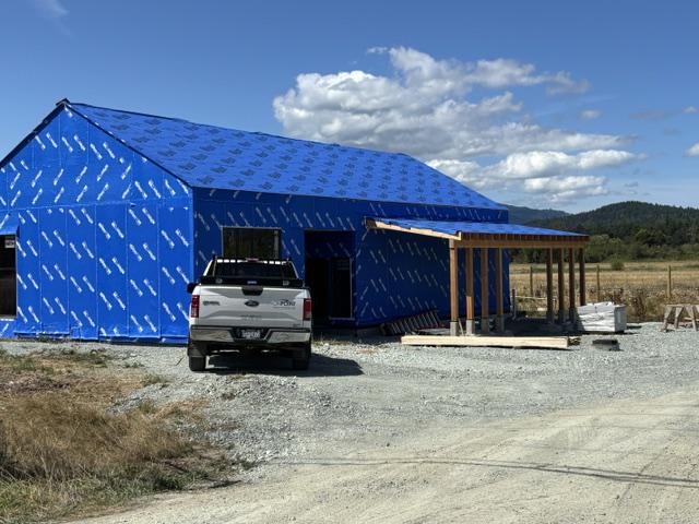 An unfinished building with a wooden awning and its exterior wrapped in blue housewrap
